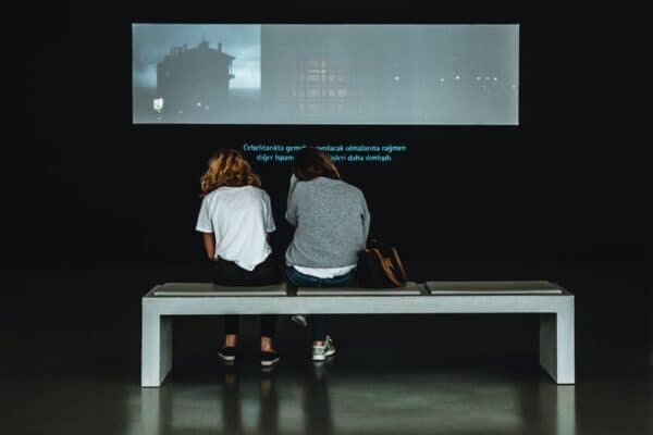 Two people sit in front of a projected display reading captioning