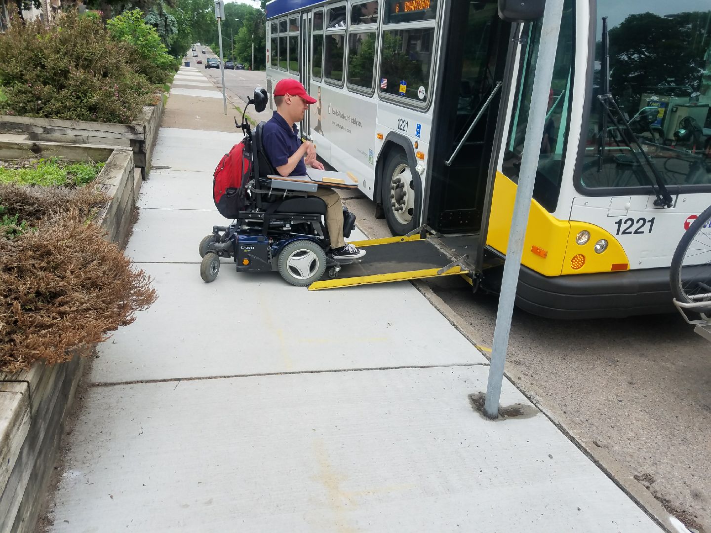 Sam Graves driving his power wheelchair onto city bus wheelchair ramp